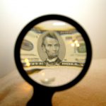A five-dollar bill shown in a magnifying glass.