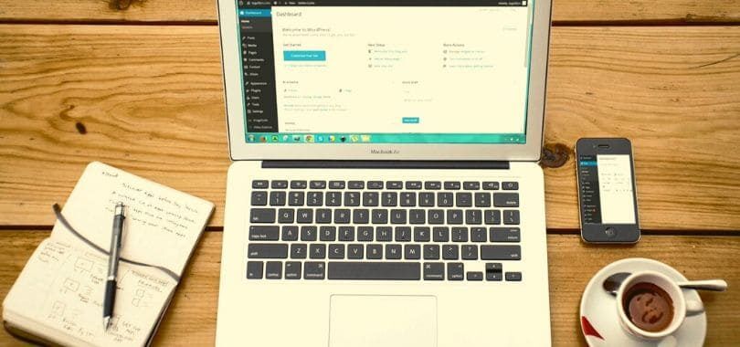 A laptop with a notebook and a cup of coffee beside it.