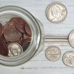 A jar of coins with four coins scattered on the side.