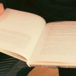 A student holding an open textbook in their lap.