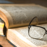 An open textbook with a pair of glasses resting on top of the pages.