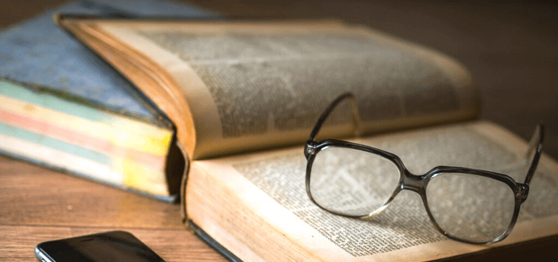 An open textbook with a pair of glasses resting on top of the pages.