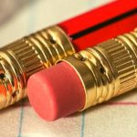 Two red pencils with erasers laying on a lined piece of paper.