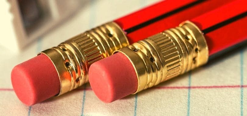 Two red pencils with erasers laying on a lined piece of paper.