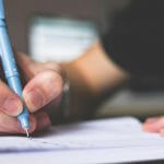 A student holding a pen and writing on a notebook.