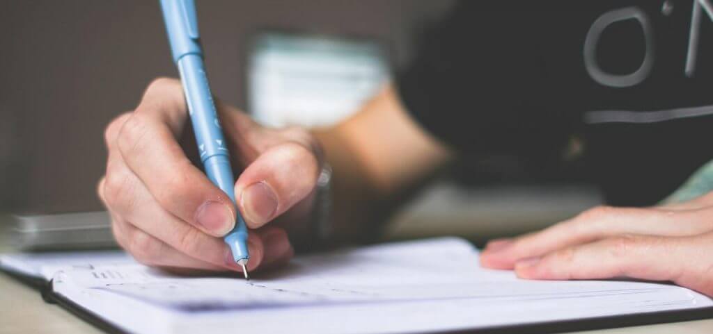 A student holding a pen and writing on a notebook.