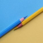A blue and yellow pencil parallel to each other, with a blue and yellow background.