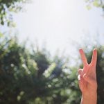 Raising hand peace sign against the trees.