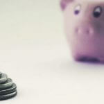 A few coins stacked together with a piggy bank in the background.