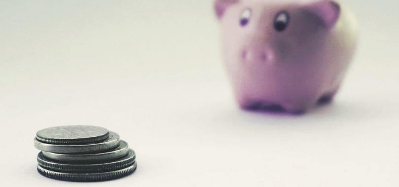 A few coins stacked together with a piggy bank in the background.