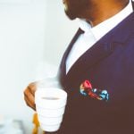 A man wearing corporate suit holding a hot cup of coffee, shown from shoulder to chest.