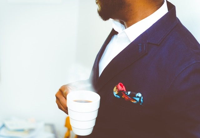 A man wearing corporate suit holding a hot cup of coffee, shown from shoulder to chest.