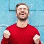 An excited person wearing a red sweater and standing against a blue background.