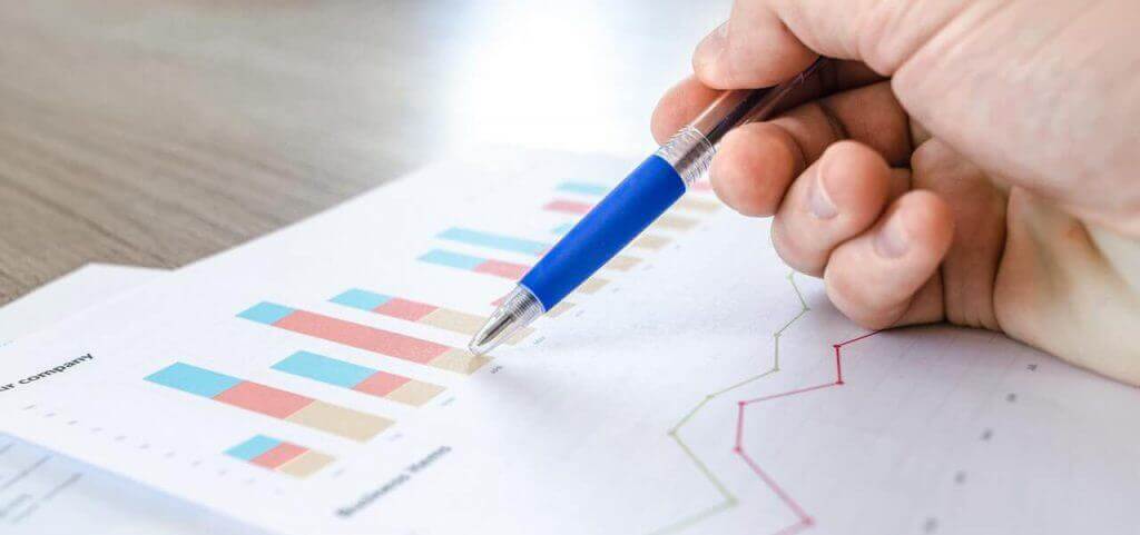 A person holding a pen on top of a printed bar graph.
