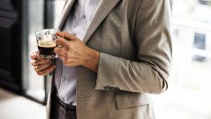 A man wearing corporate suit holding a hot cup of coffee, shown from shoulder to waist.