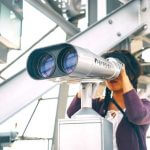 A student looking through a pair of binoculars.