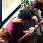 Students leaning against a window ledge on their phones.