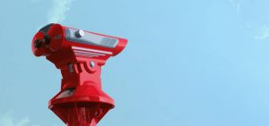A pair of red binoculars outside against a blue sky.