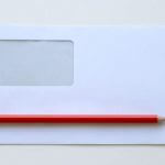 An empty white envelope with a red pencil sitting on top of it.
