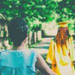 A mother watches her graduating daughter walk down a road.