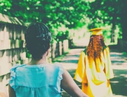 A mother watches her graduating daughter walk down a road.