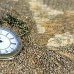 A pocket watch laying in sand on a map.