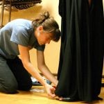 A woman kneeling and fixing the model's black dress.