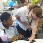 A teacher is looking at the student's paper on the desk.