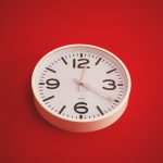 White wall clock against red background.