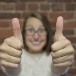 Girl with eye glasses with a big smile while showing two thumbs up.