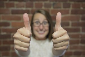 Girl with eye glasses with a big smile while showing two thumbs up.