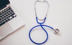 Blue stethoscope next to a laptop.