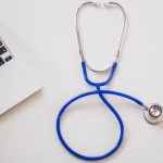 Blue stethoscope next to a laptop.