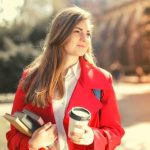 A student wearing a red blazer, holding a cup of coffee and books.