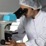 A scientist in a lab coat looking into a microscope.