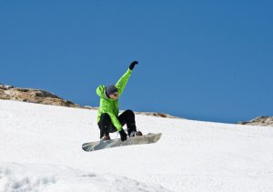 A man wearing a green coat is snowboarding in mid-air.