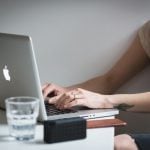 Student sitting at her dorm desk typing an essay on her Macbook.