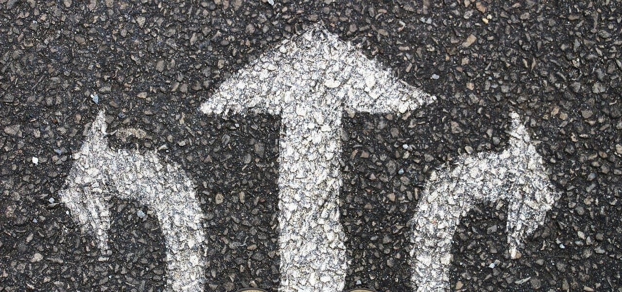 Three white arrows pointing in different directions, printed on black asphalt.