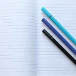 An open notebook with three pens on top of it.