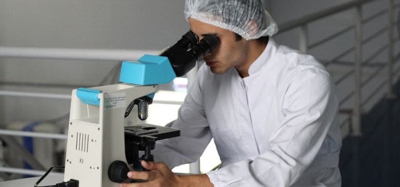 A scientist in a lab coat looking into a microscope.