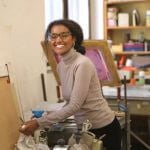 A student smiling, standing by a table.