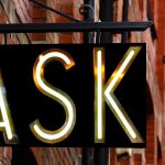 A sign that says "ask" with a light fixture next to it.
