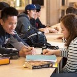 Students talking to each other with books on their desks.