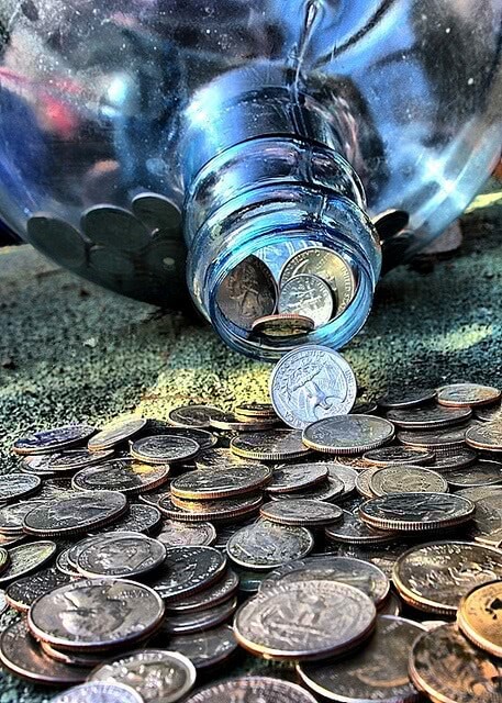 Coins are spilling from a glass jar.