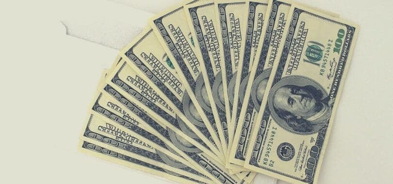 A fan of one hundred dollar bills on a gray background.
