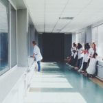 A white hospital hallway with people standing at the far end.