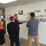 A man is pointing his hand on the whiteboard with images on it while discussing to three people.