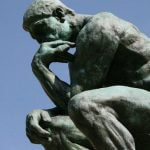 A statue of the Thinker against a blue sky.