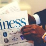 A person holding a newspaper with "business" printed on it.