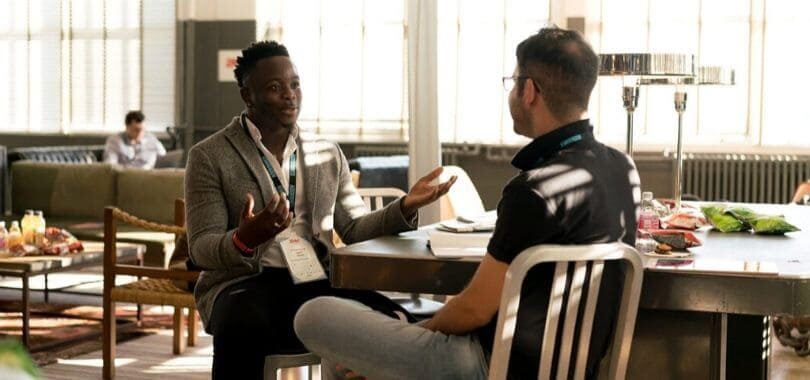 Two students talking to each other at a table.